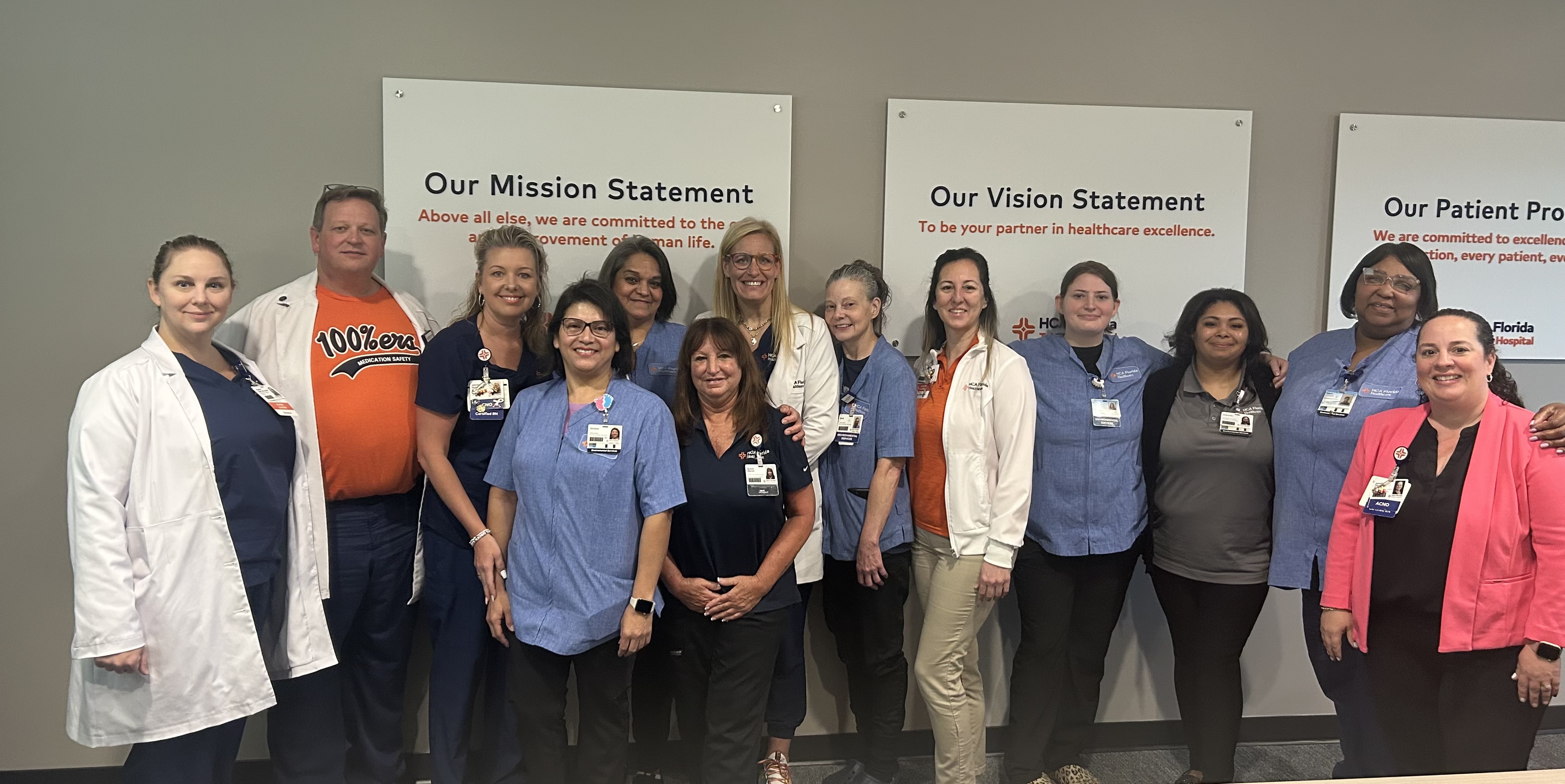 A group of HCA Florida Trinity Hospital colleagues standing together against signs with their mission and vision statements