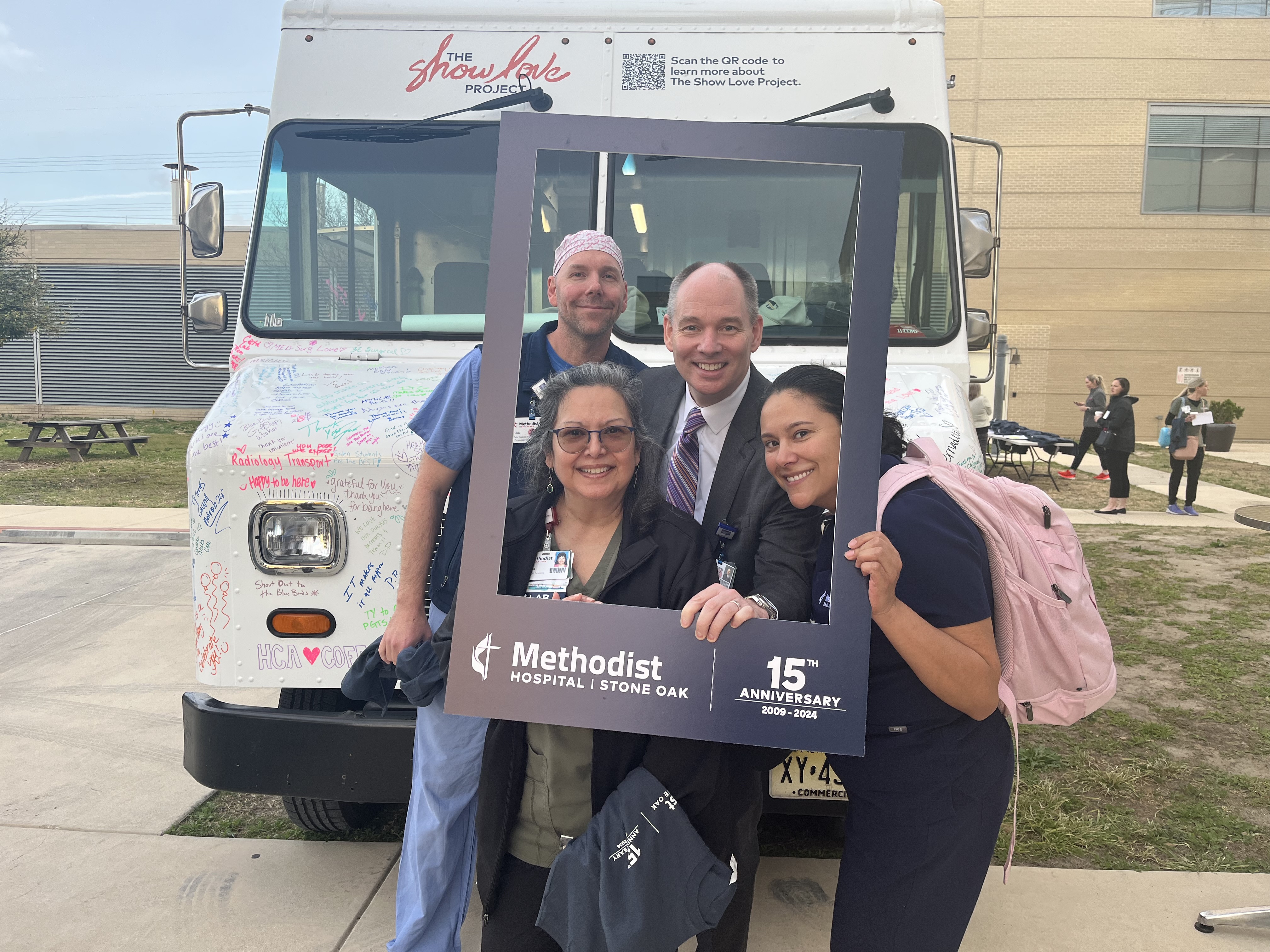 Four hospital staff members pose behind a picture frame cutout that reads 'Methodist Hospital Stone Oak, 15th Anniversary.'