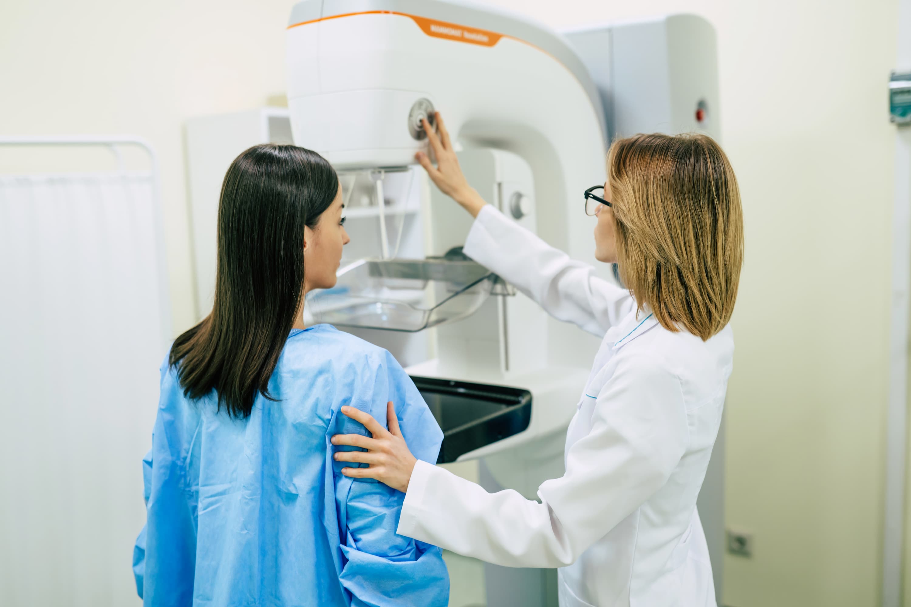 A doctor assists a patient with a mammogram screening, adjusting the imaging machine.