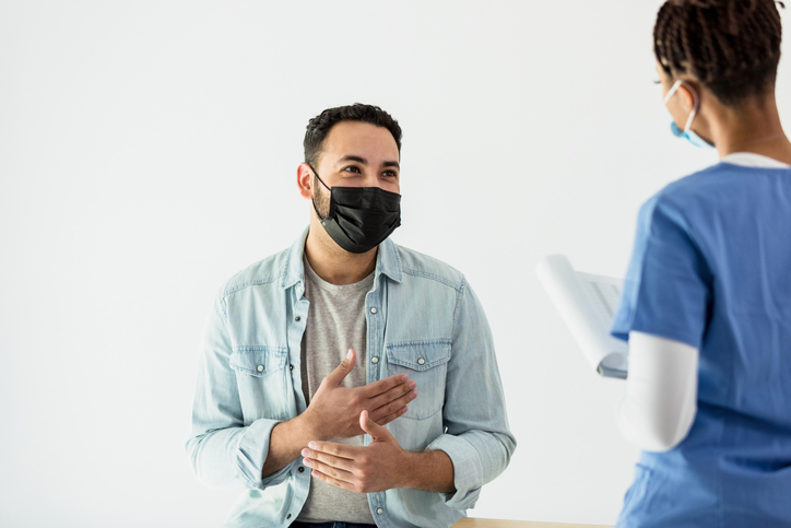 A man smiles while wearing a face mask, talking with a medical professional during an exam.