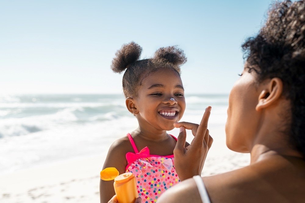 A woman applies sun screen to a young girl's face on the beach