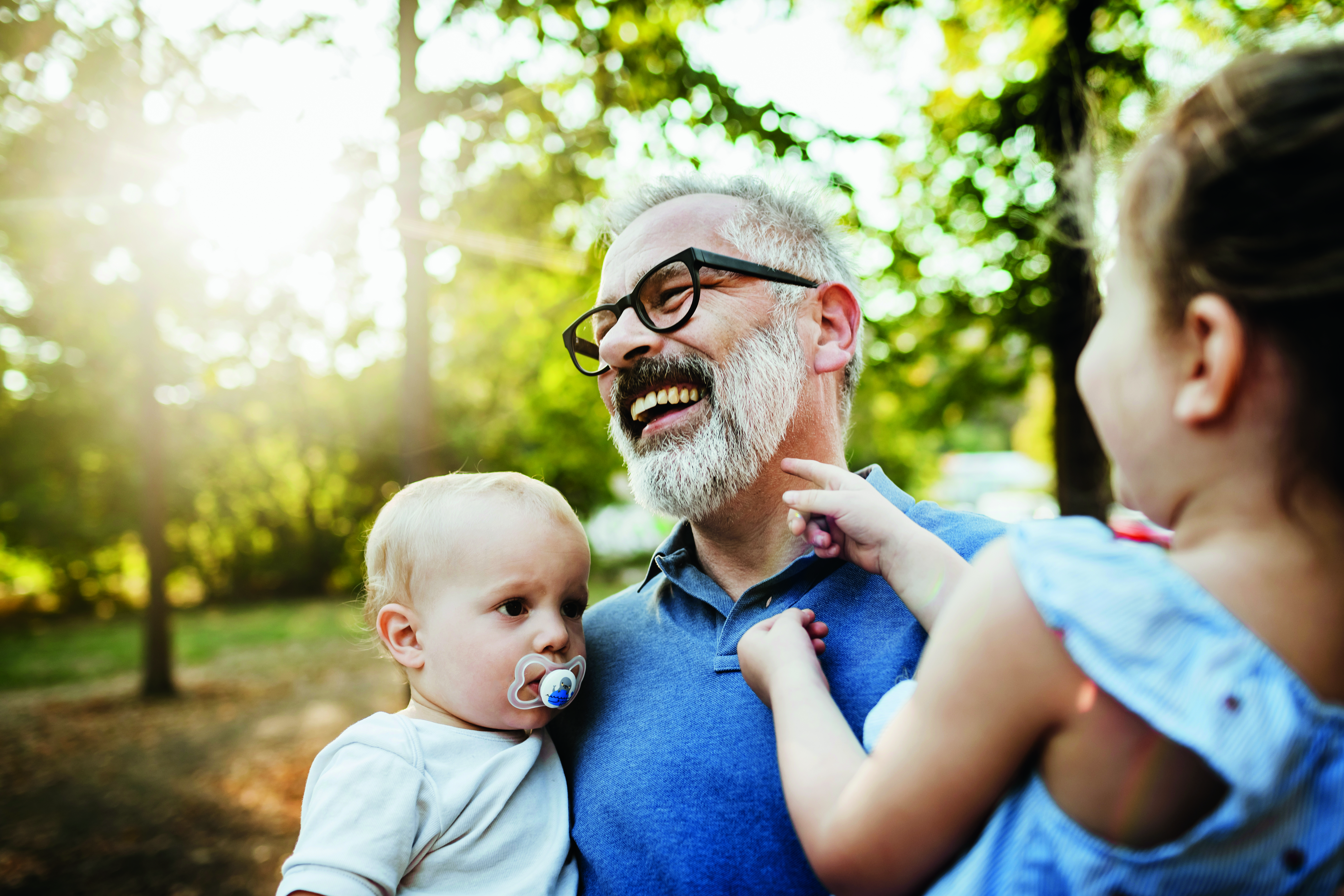 Two children having fun with their grandpa while on a day out at the park together.