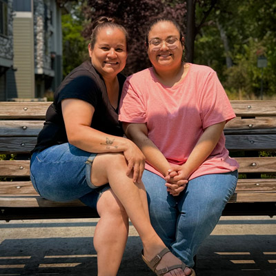 Bianca and Marisol Valdez sitting together on a park bench outside.