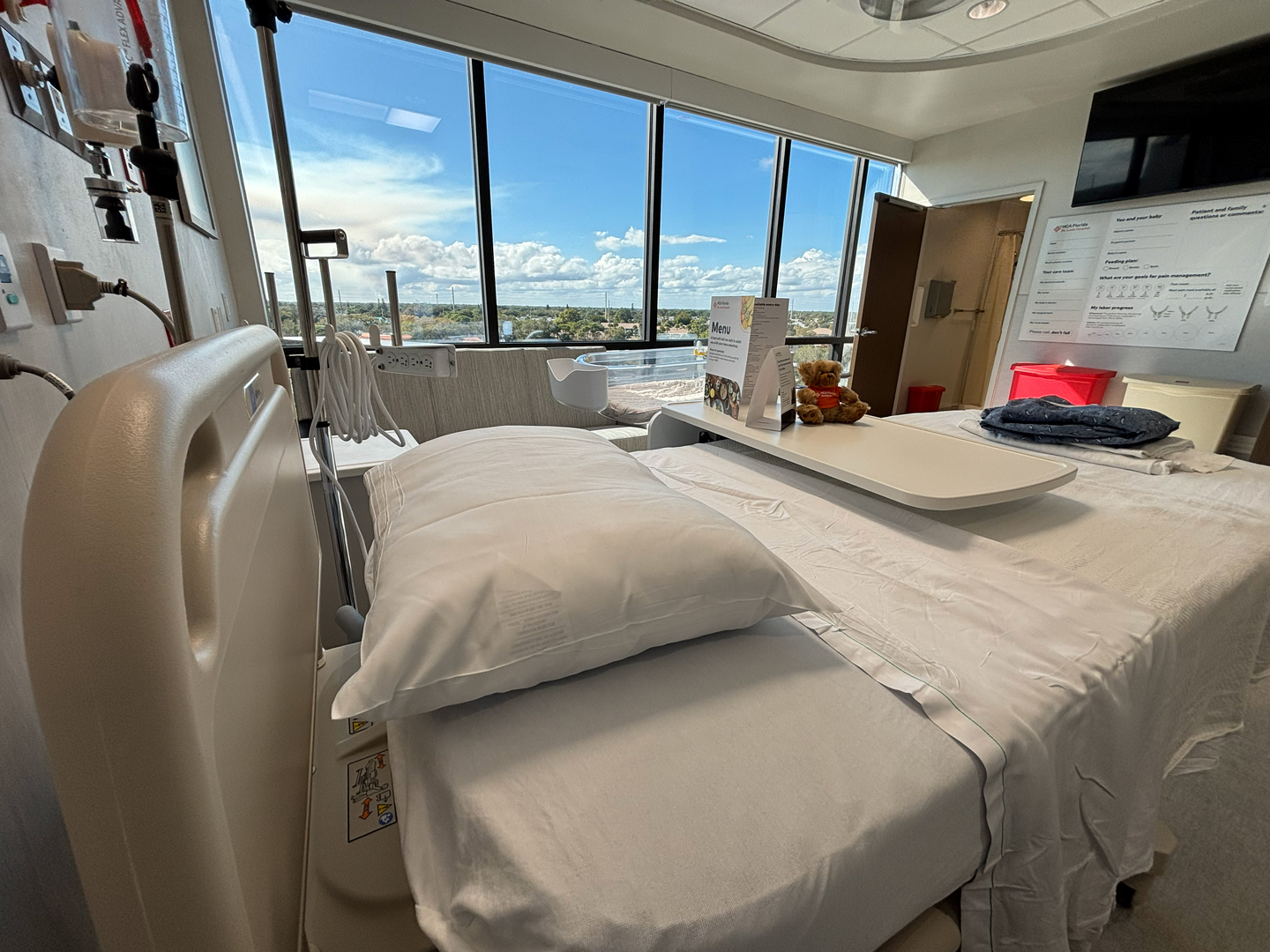 Labor and delivery room at St. Lucie Hospital, with a patient bed and a wall-mounted television.