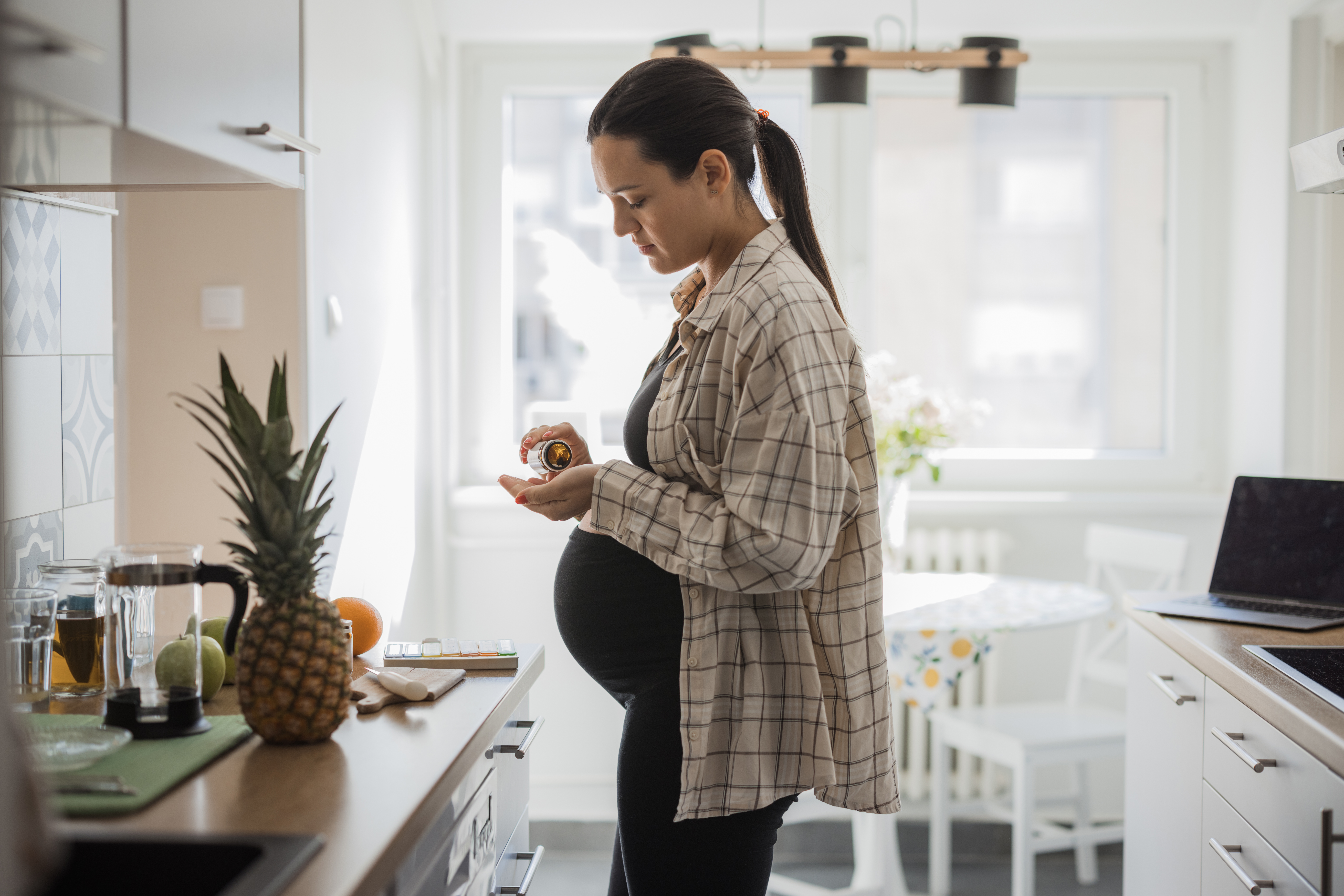 A pregnant woman standing in her kitchen, taking prenatal vitamins.