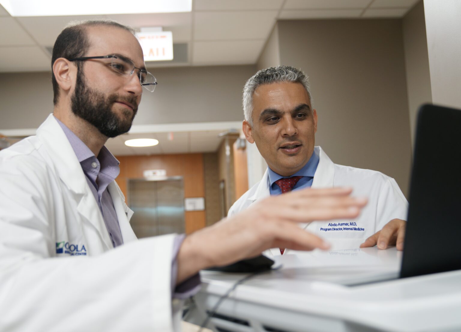 Two physicians in white coats standing next to a computer station in a hospital