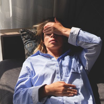 Woman lying on a couch holding her head and her stomach.