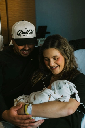 Morgan Johnson is smiling while holding her baby, with her husband by her side.