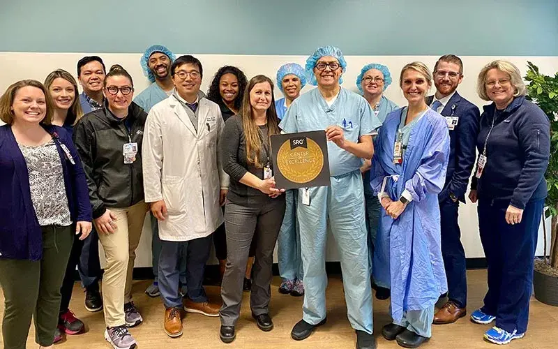 Riverside Community Hospital medical professionals smile while holding an award from SRC for being a Center of Excellence in robotic surgery.