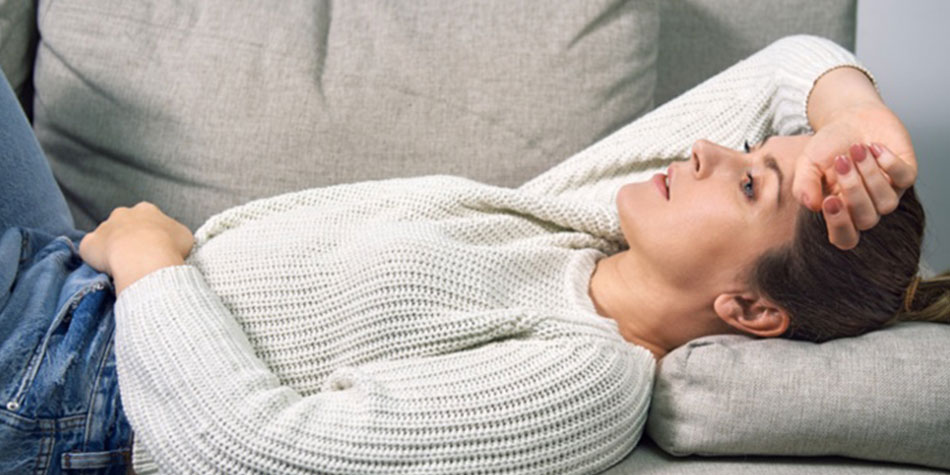 A woman lies on her back on the couch, holding her stomach.