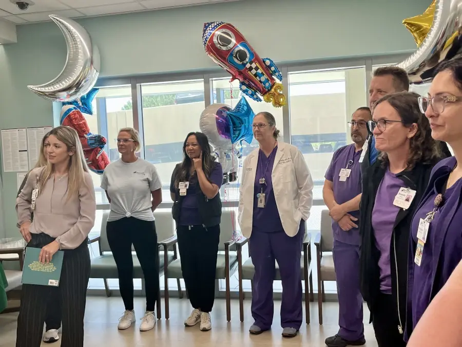 Male and female hospital staff standing with balloons welcoming young former patient.