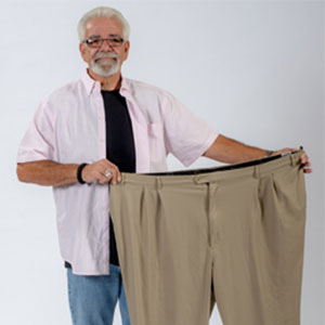 Steve Scholar smiles while holding up a pair of pants that he used to wear prior to weight loss surgery.