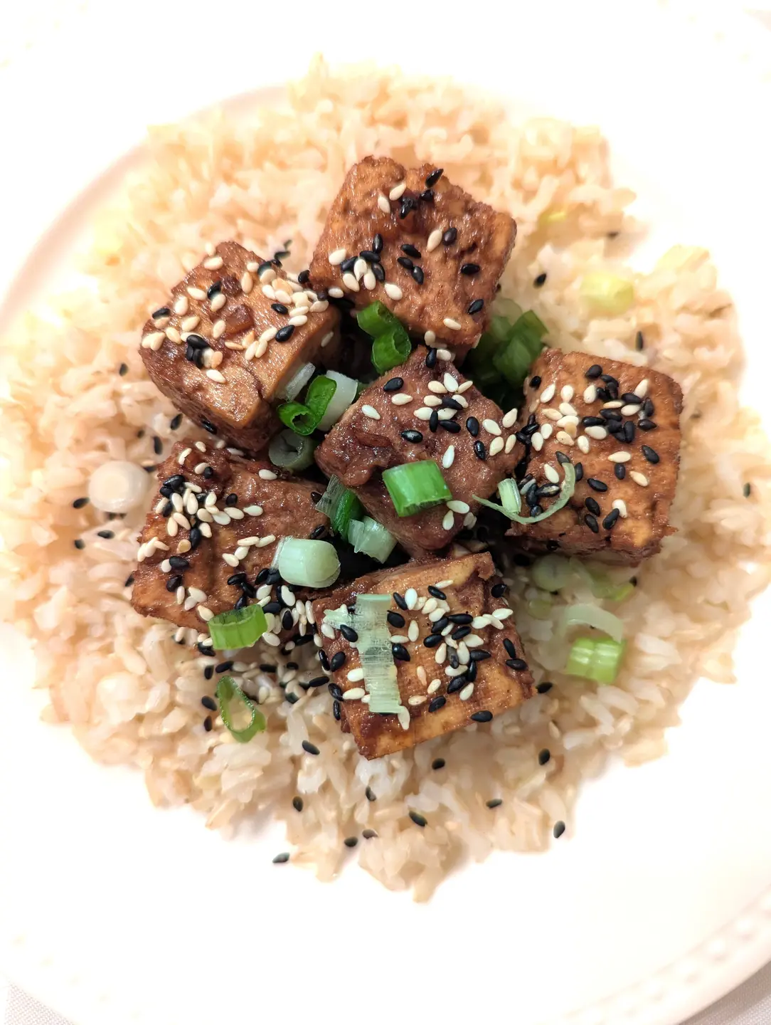 Fried tofu topped with black and white sesame seeds and scallions, on a bed of white rice.