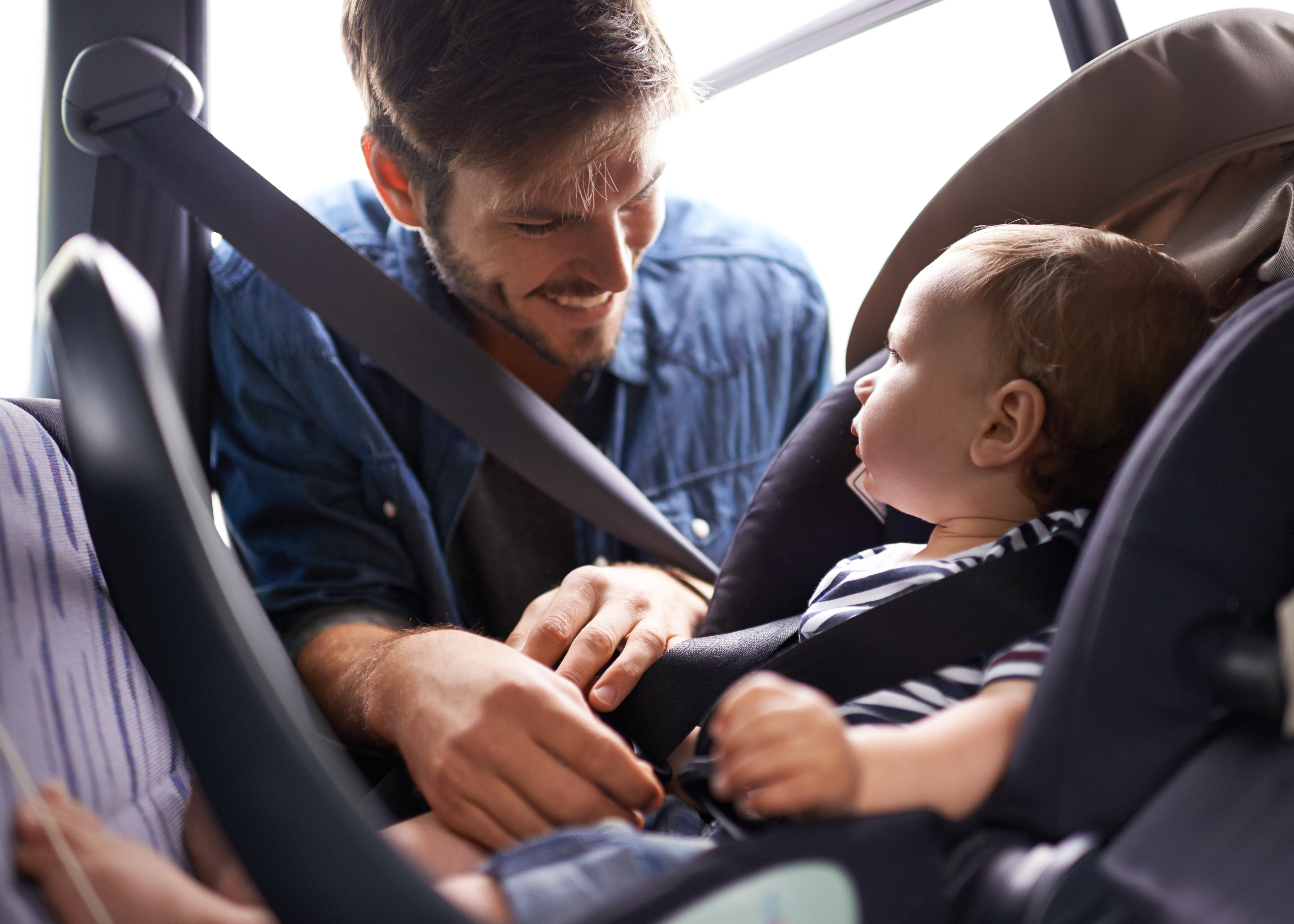 A man fastens a toddler into a a child safety seat in a car