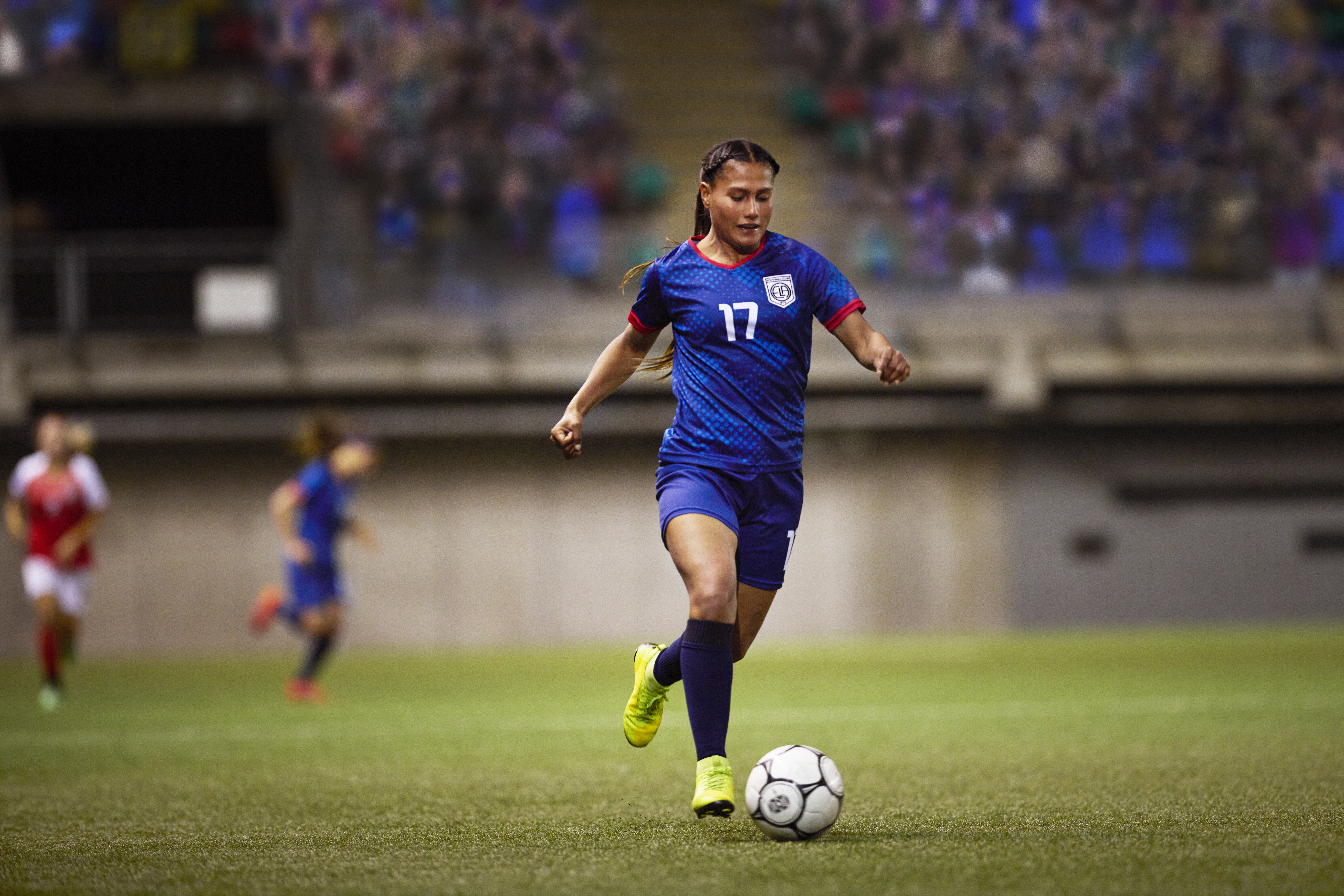 A soccer forward dribbles the ball up pitch during a break away play, as the opposing team chases after her.