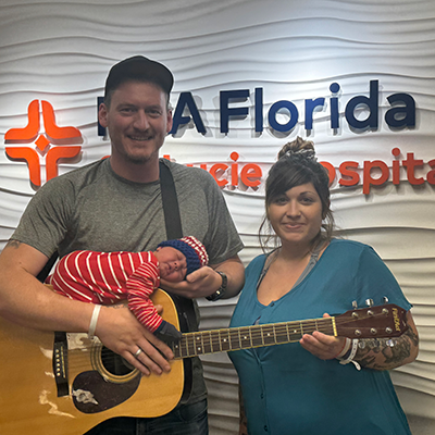 Colton, Rebecca and their newborn posing with a guitar.