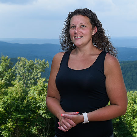 Heather Umberger poses in front of a treelined mountains on a sunny day