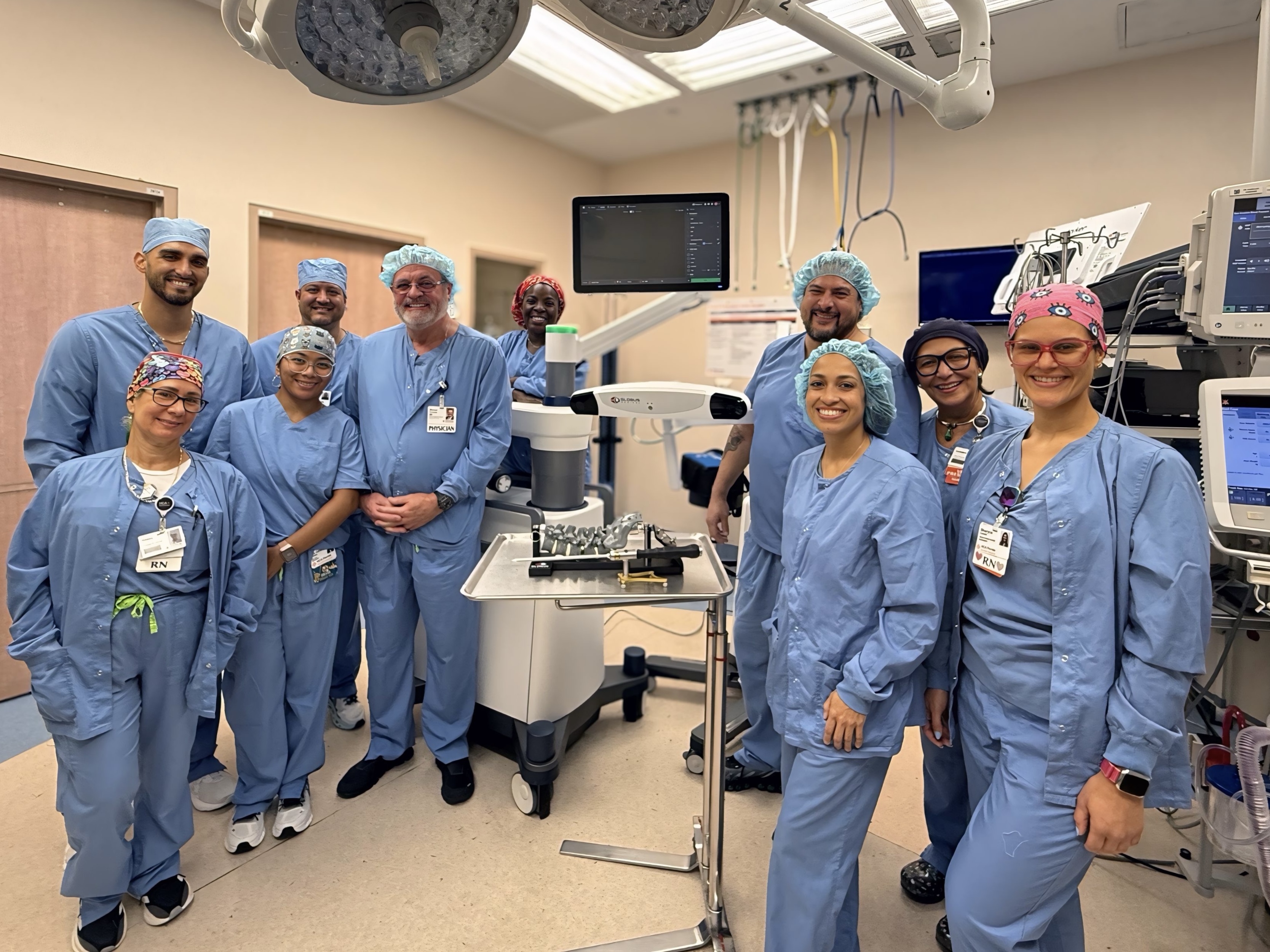 A group of people — the Team FROMKE of HCA Kendall Hospital with the newest robotic system on the background — posing and smiling for the picture.