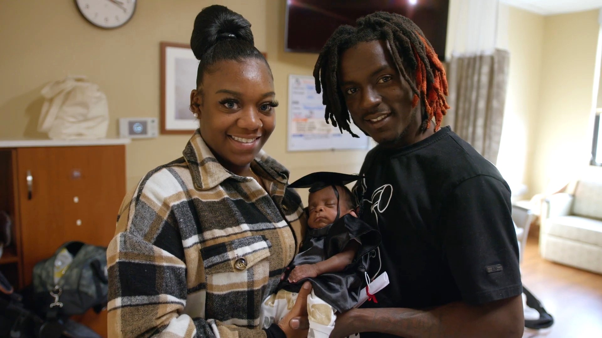 Raven and her partner hold baby Jakai, who wears a little NICU graduation cap.