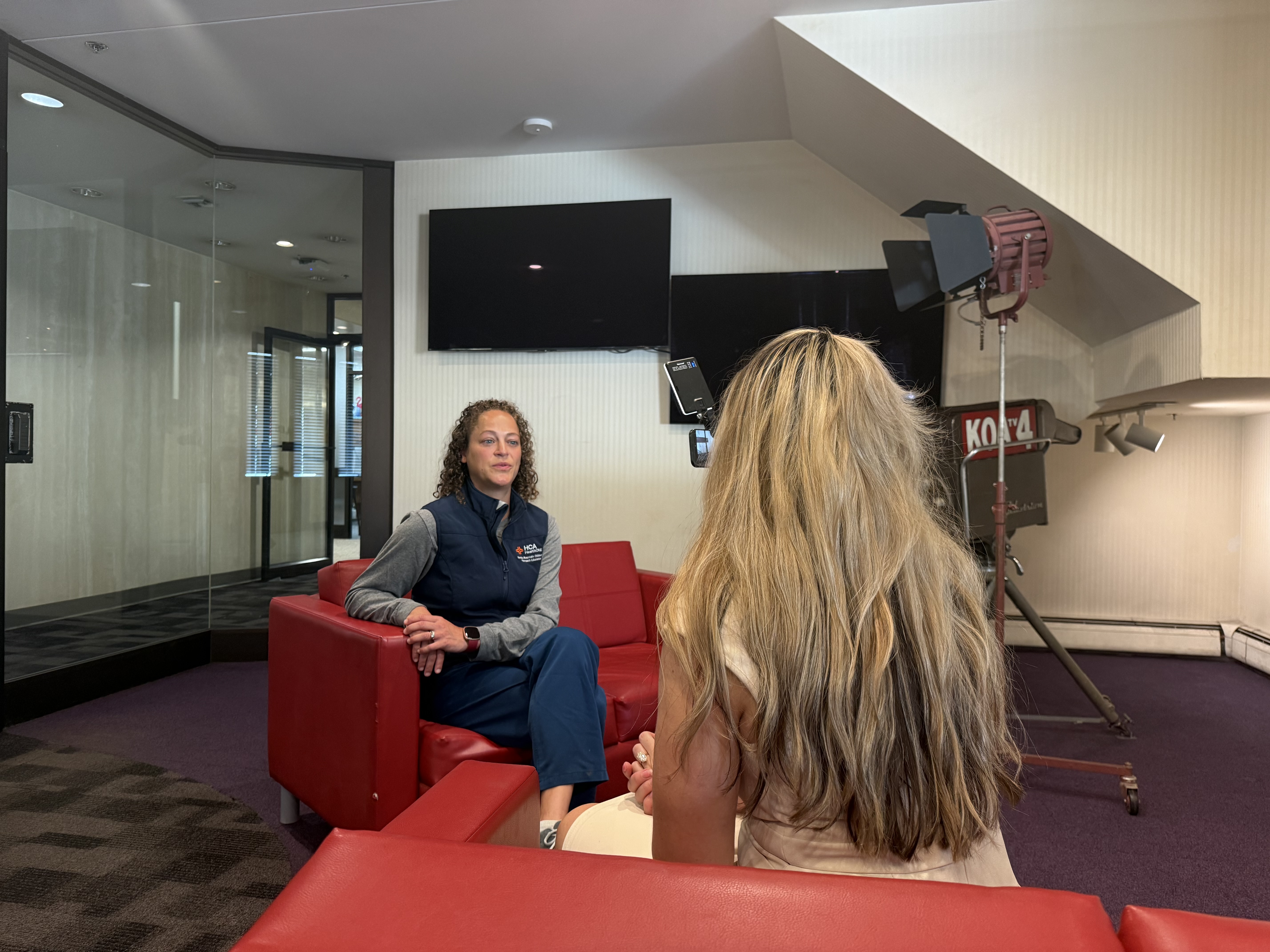 Dr. Danielle Dhaliwal sits on a red couch during an on-camera interview with a reporter.
