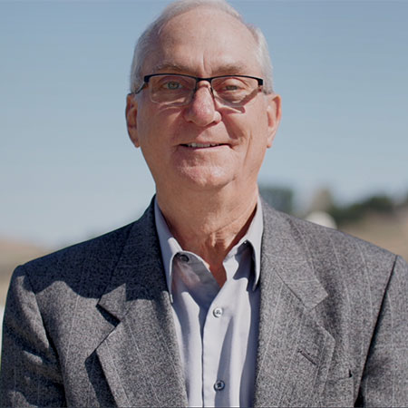 Senior cancer survivor Garret Nancolas wears eyeglasses and a suitcoat and smiles outdoors.  