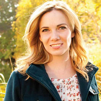 Lara Hays smiles while standing outdoors in front of grass and trees.