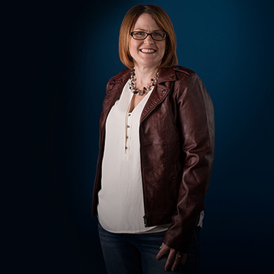 Heather S. wearing a maroon leather jacket and smiling.