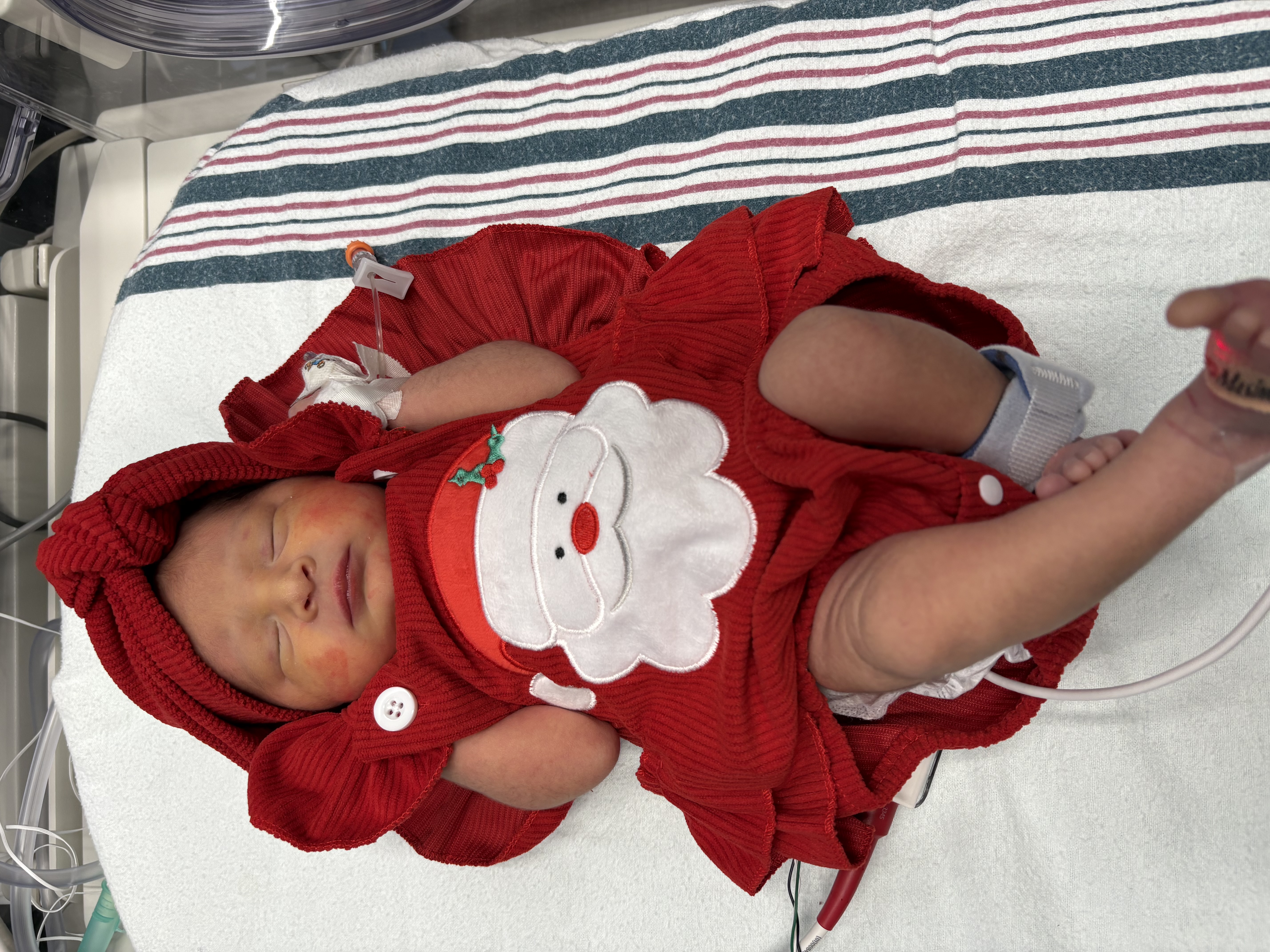 Newborn in crib dressed in Santa onesie.