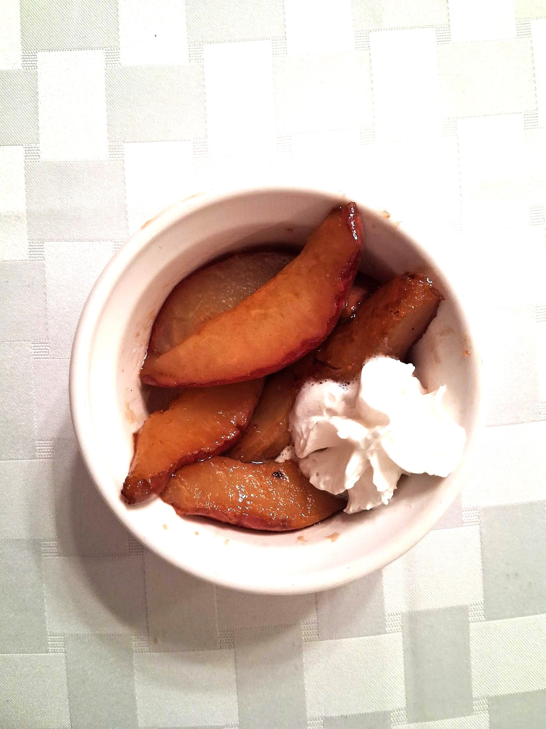 Caramelized pears with whipped cream in a white bowl, on a tablecloth.