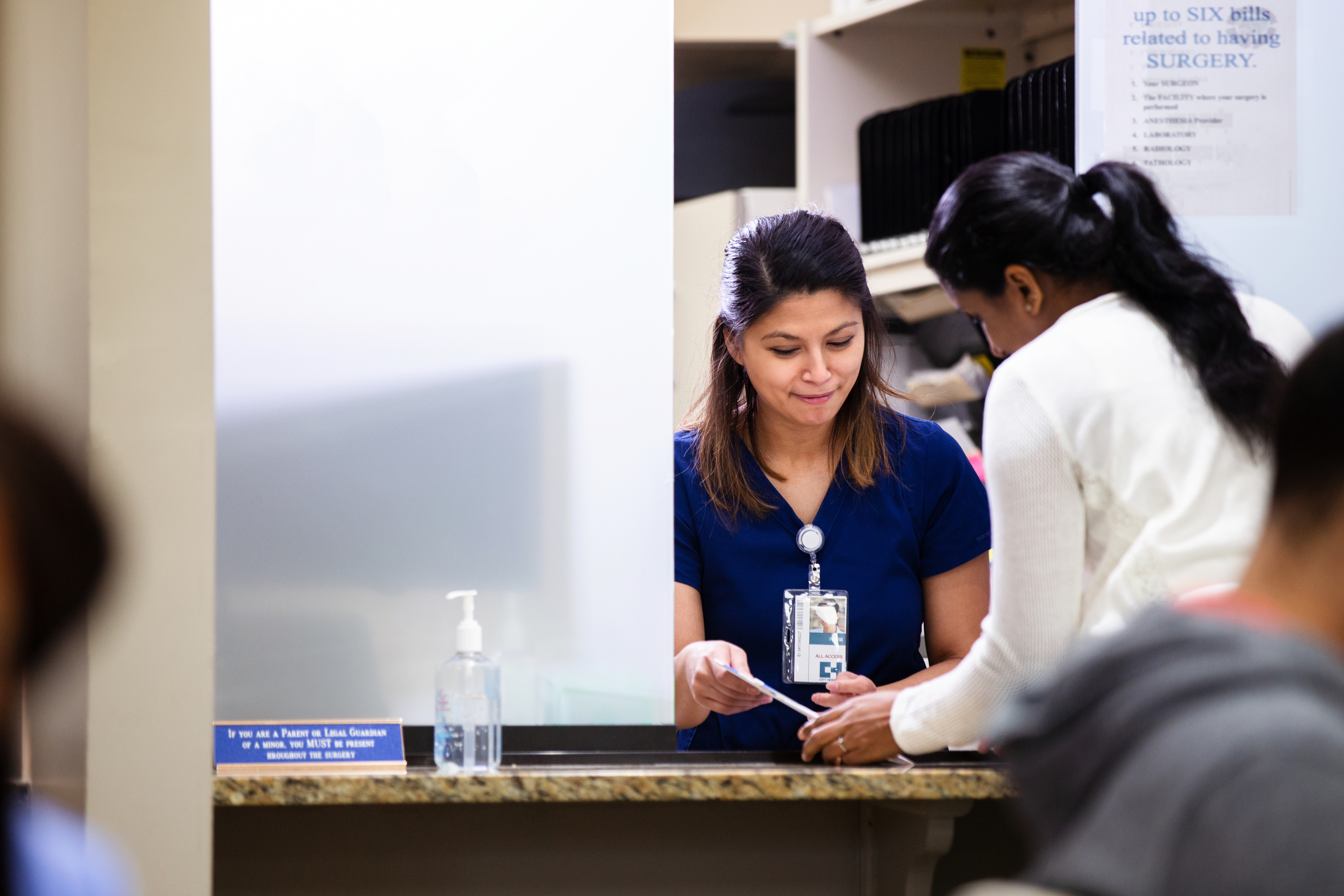 Two women dressed in hospital uniforms look down at paperwork at a counter
