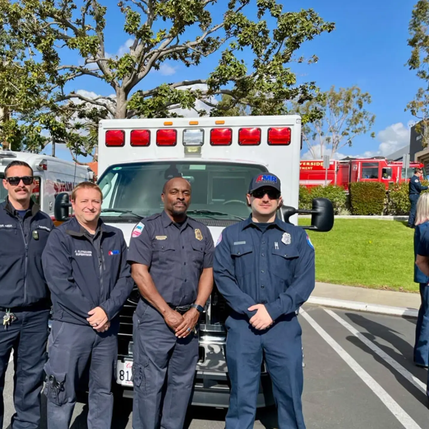 A group of four medical professionals smile while standing together in front of an ambulance.