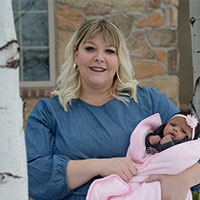 Sarah Dibba smiles while holding her daughter, Kaiyah, in front of their house.