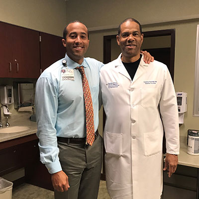 Radiation oncologists, David Randolph II and David Randolph standing next to each other in an exam room.