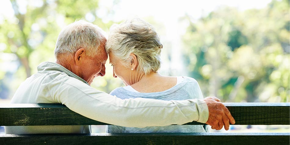 Senior couple, sitting outside on a bench, embrace.