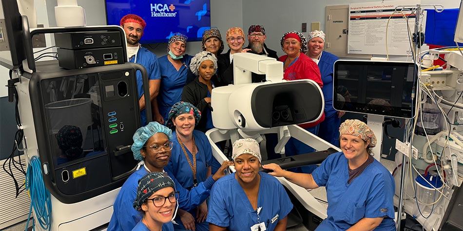 A group of surgical staff surround robotic surgical device in operating room
