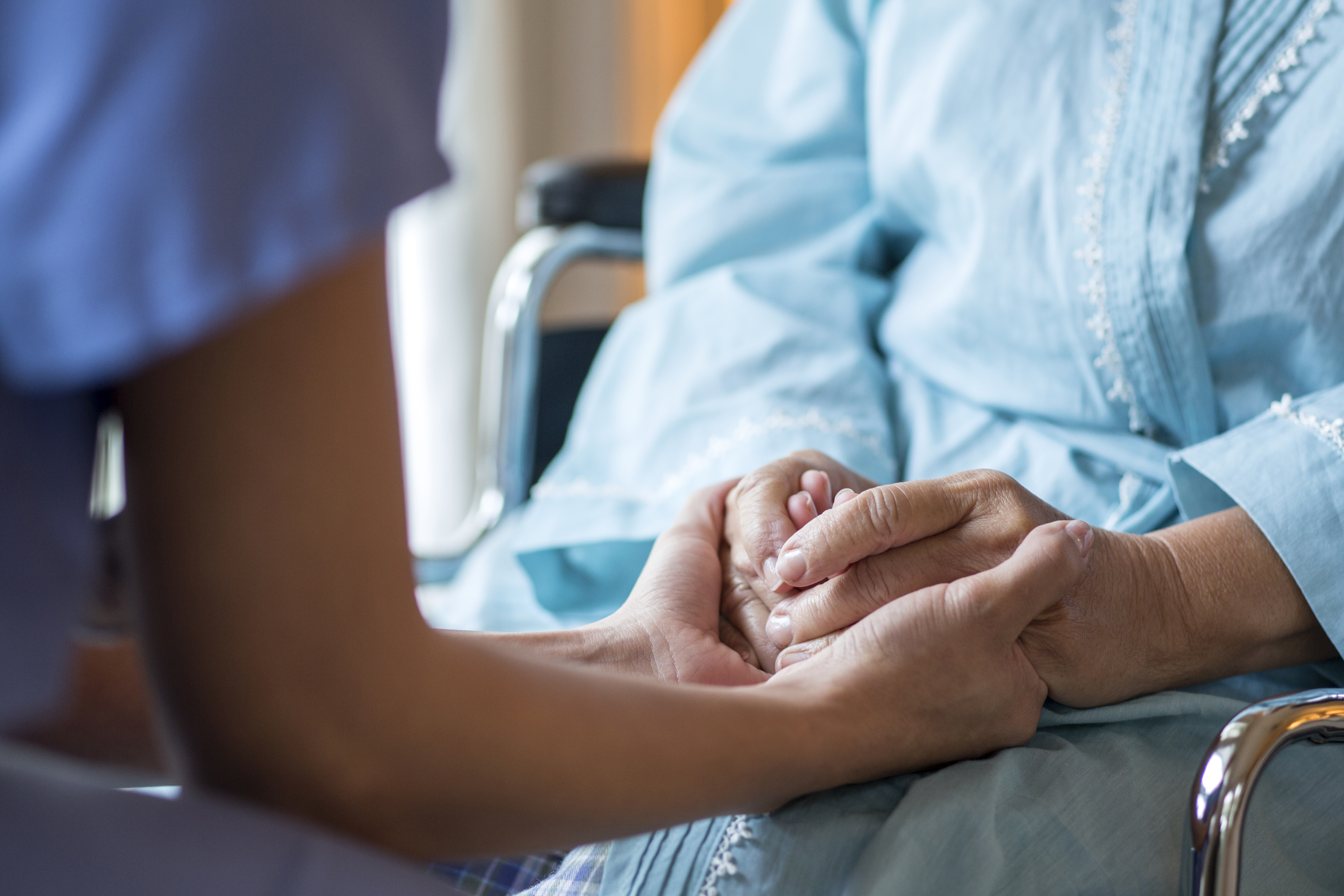 A nurse comforting an older patient in a wheelchair.