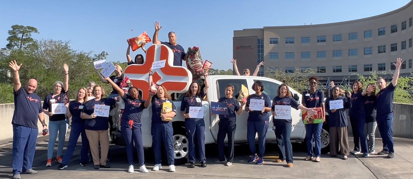 For We Show Up®, combined Nursing Administration/Quality/Risk Management and a other teams share their glee and pose before a full truck load of food and toys for the Jacksonville Humane Society