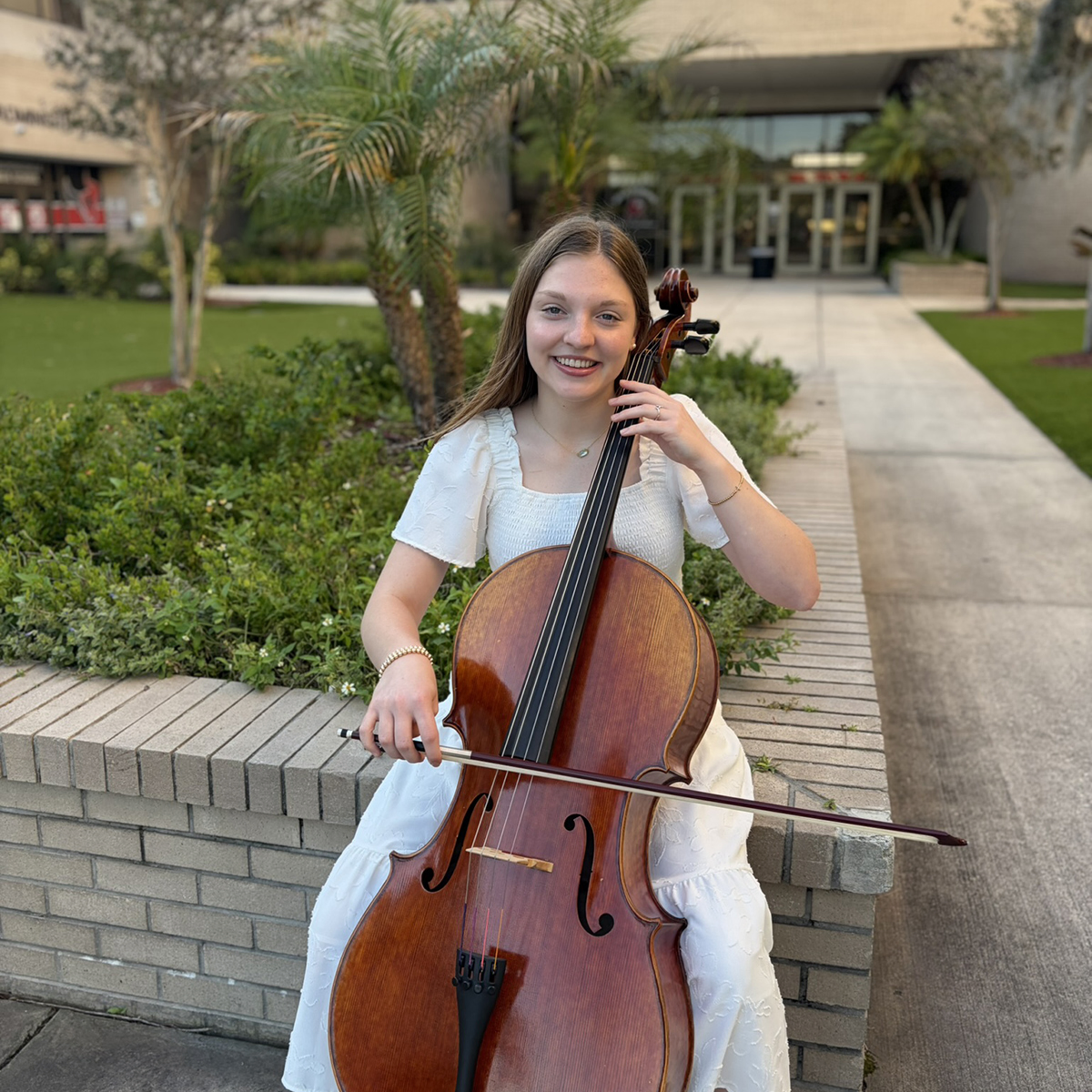 Kate Lantz plays cello in front of high school.