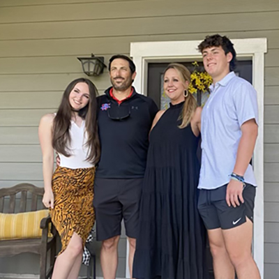 Toby Wise smiles while hugging his wife and two teens on their front porch.