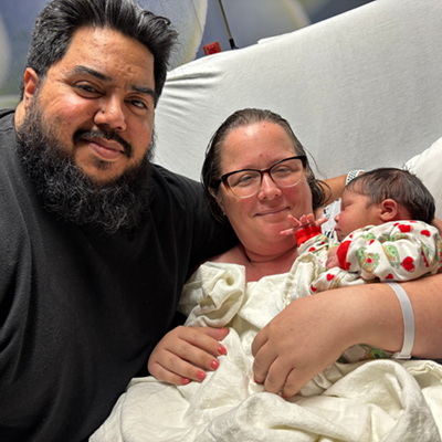 Elisha and Angel holding a baby while in a hospital bed.