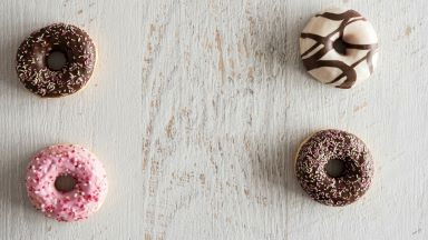 Four frosted donuts on a white wooden table.