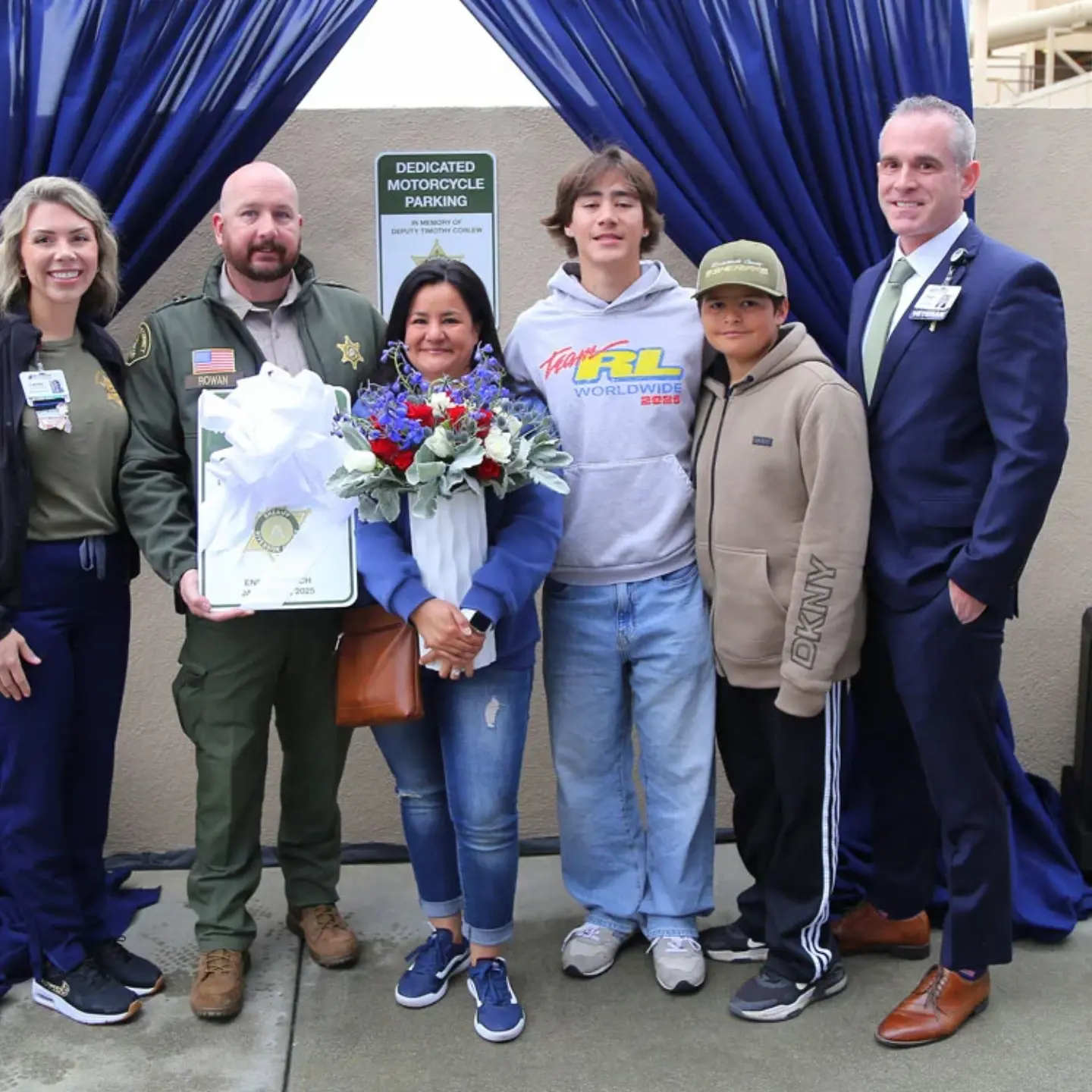 Lacey Page, Justin Rowan, Peter Hemstead and Timothy Corlew's family smile while standing in front of a dedication plaque.