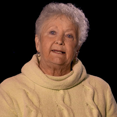 Carolyn Cook smiles during an interview while wearing a yellow knit sweater and gold hoop earrings.