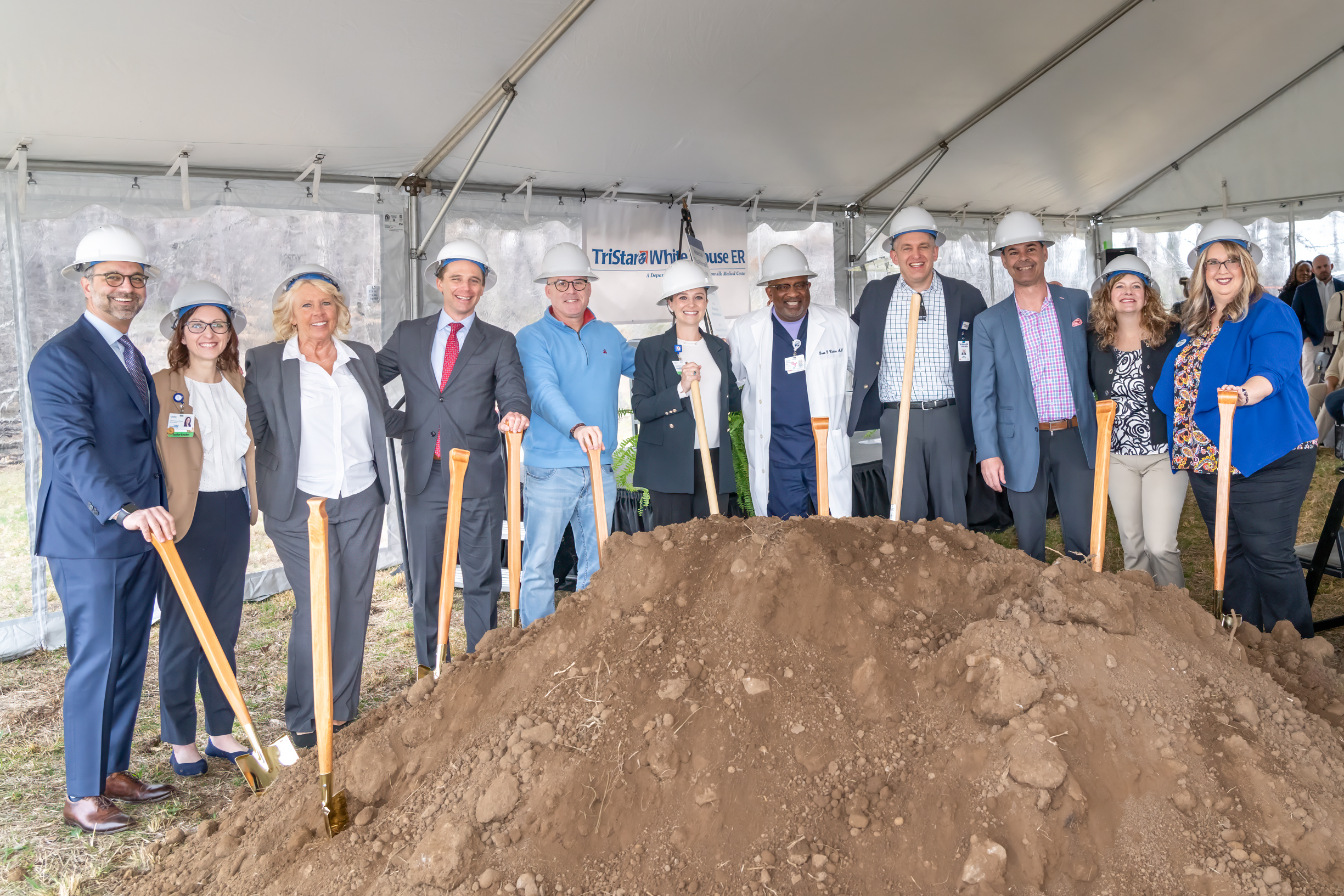 Large group of Tristar staff standing next to a large pile of dirt while wearing hardhats and holding shovels.