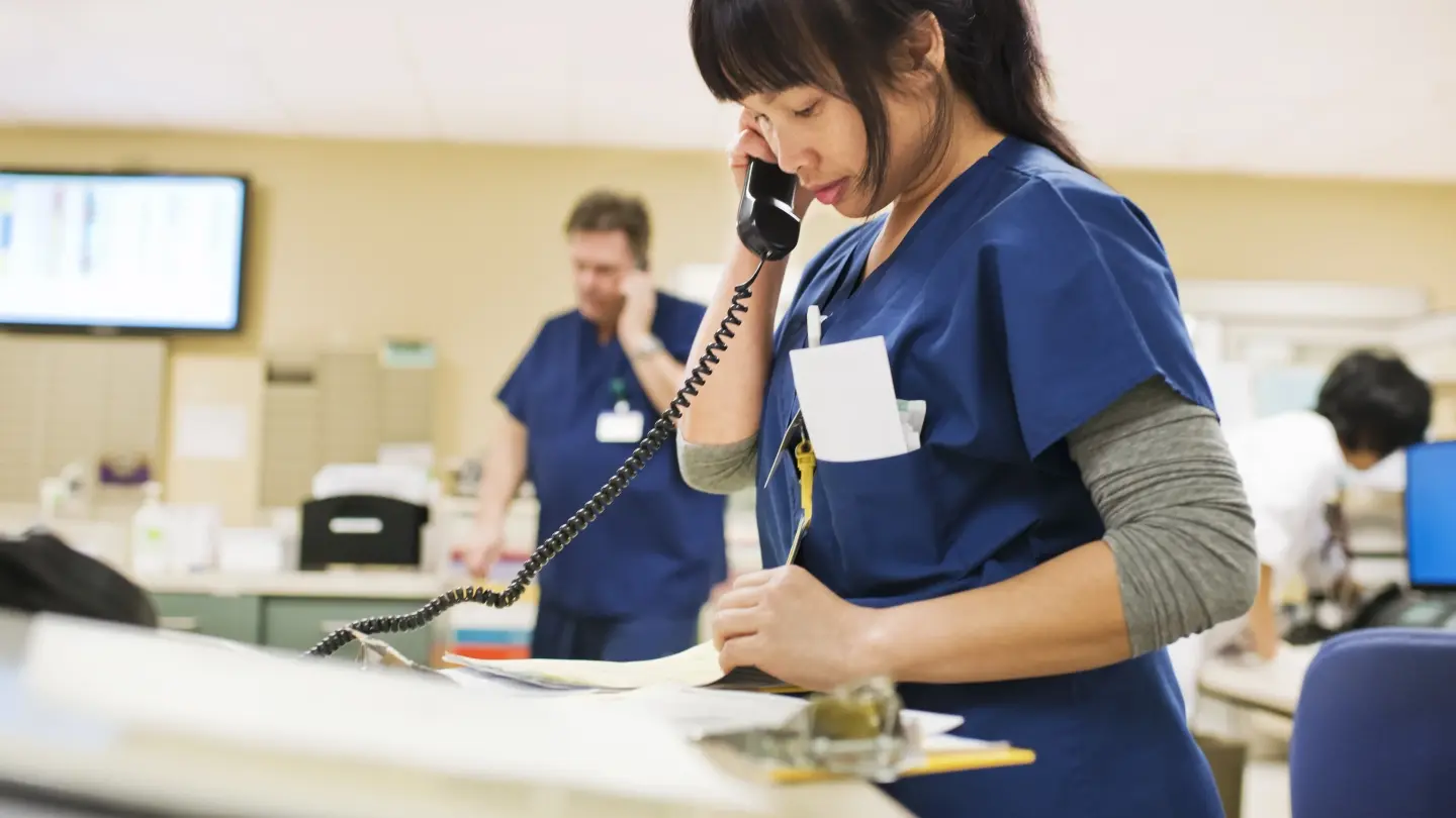 Female nurse looking at paperwork while talking on the phone.