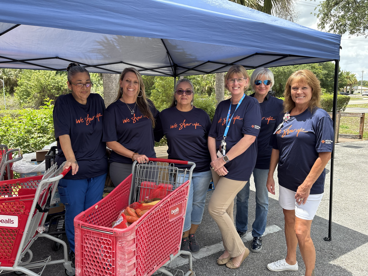 Colleagues from HCA Florida Lehigh Hospital gather with food donations and grocery carts while volunteering with Lehigh Community Services