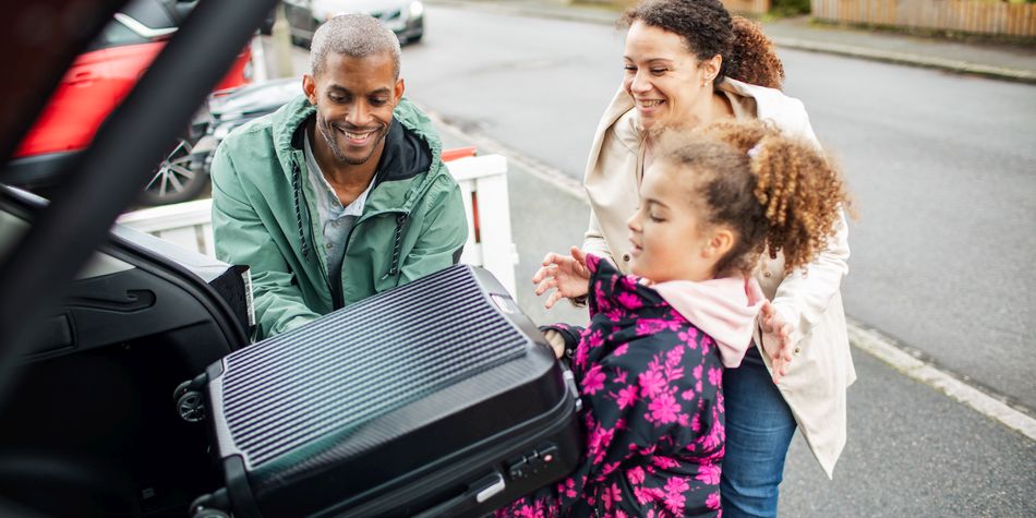 A couple smile while helping their daughter take her suitcase out of the trunk of their car.