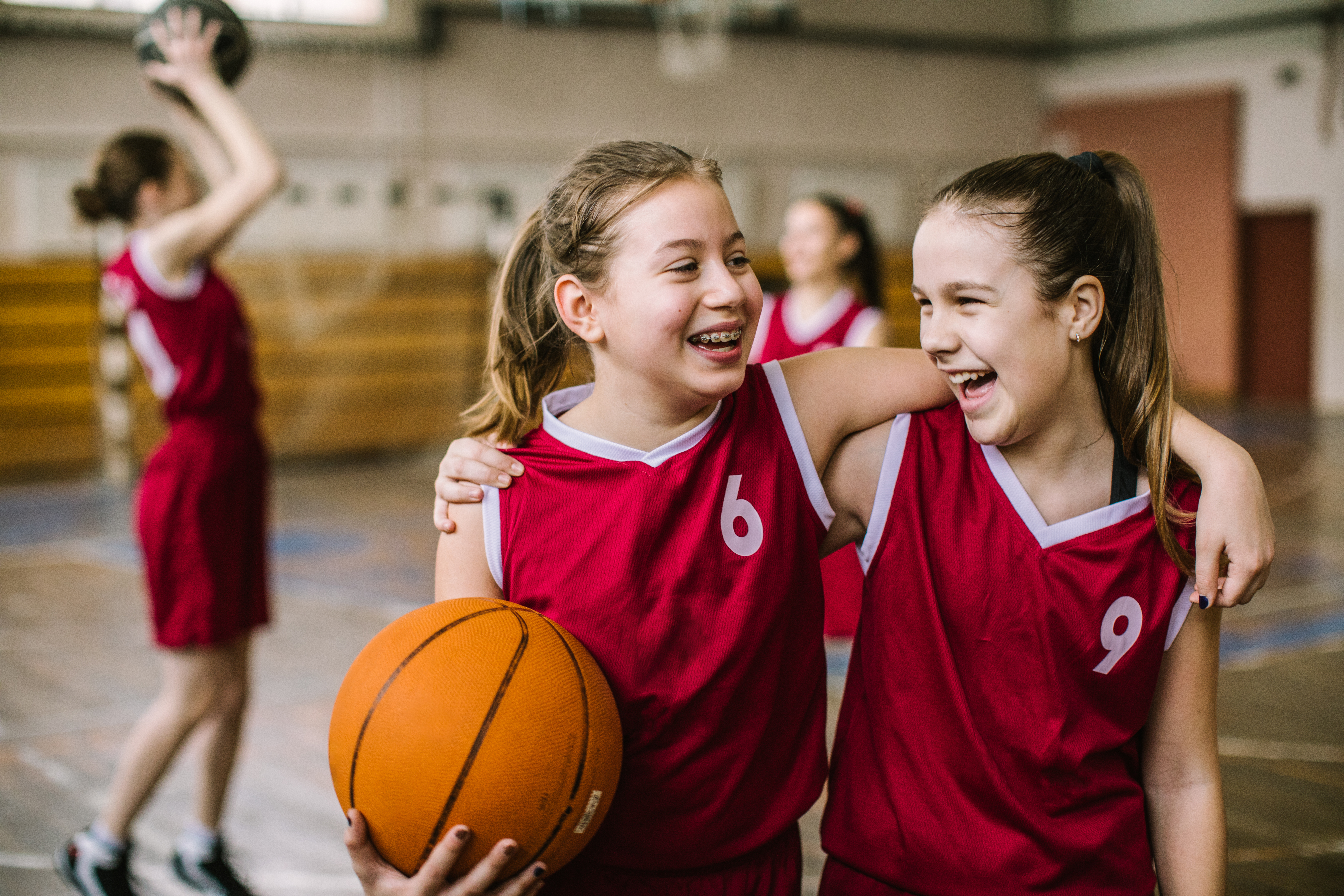 Two teen girls smile while embracing during a basketball game.