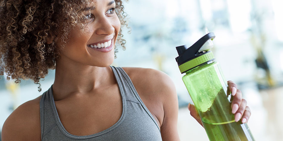 A young woman in a tank top smiling, holding a large water bottle.