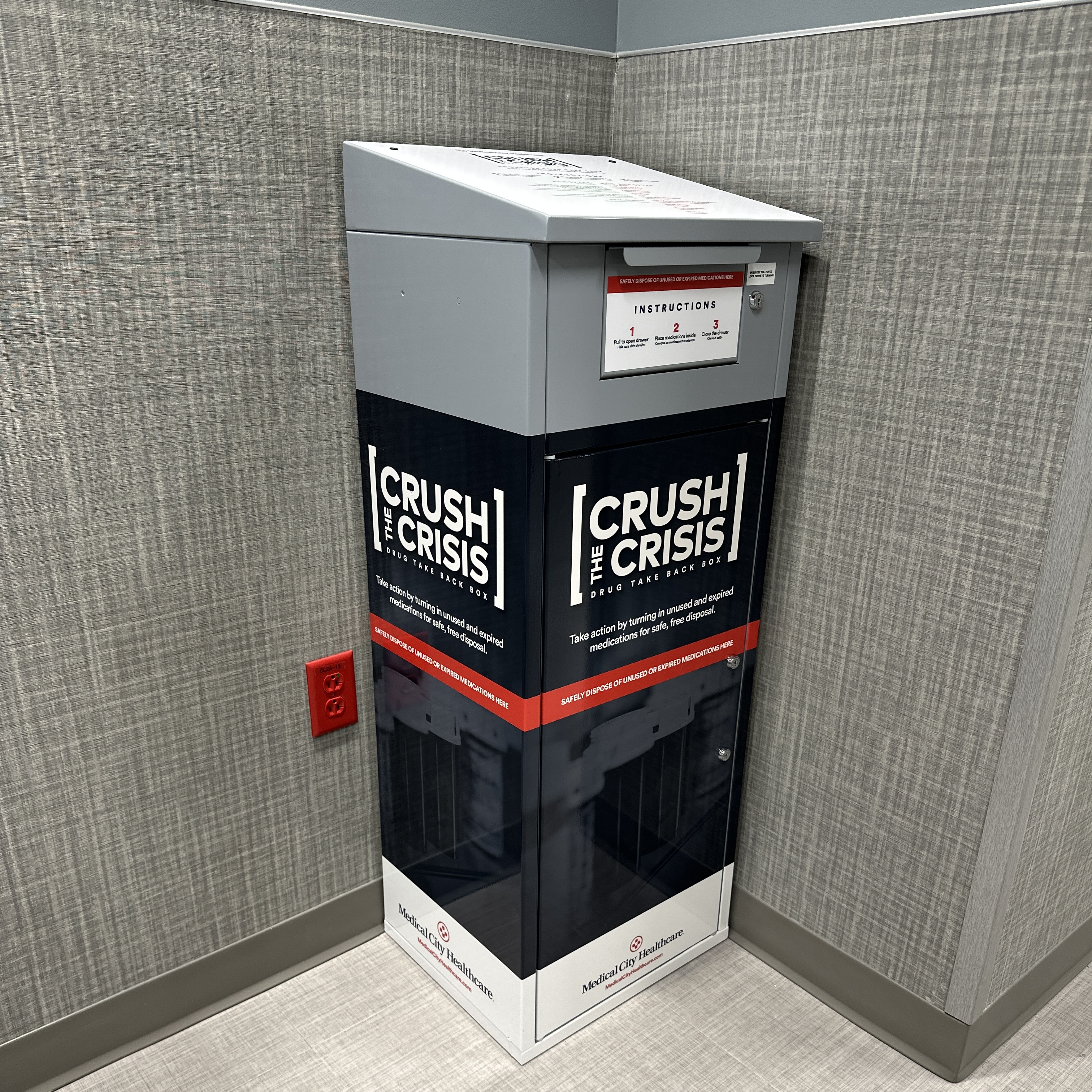 Crush The Crisis drop box at Sachse Hospital. A navy  and gray metal bin tucked into a corner.